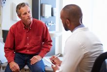 man sitting on hospital bed talking to doctor in a chair